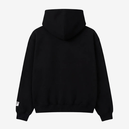 Back view flat-lay photograph of the CELESTIC Black Gemstone Hoodie on a white background. This premium heavyweight black cotton fleece pullover features a clean, minimalist back design without graphics, a structured double-lined hood, and ribbed cuffs and hem. A distinct woven CELESTIC brand patch with white text is visible on the left sleeve cuff.