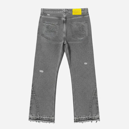 Grey flared jeans back view. Washed distressed grey denim pants highlighting a yellow Celestic brand patch on the waistband, custom embroidery on both back pockets, lower leg panel stitching, and frayed raw hems.