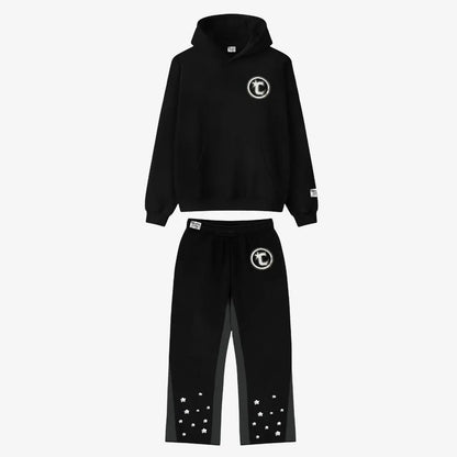 Main product image of the CELESTIC Black Star Tracksuit set. This premium heavyweight black cotton fleece ensemble features an oversized hoodie with a white circular 'C' star logo on the chest and matching relaxed sweatpants with the same logo on the thigh and multiple white embroidered stars at the leg openings. 