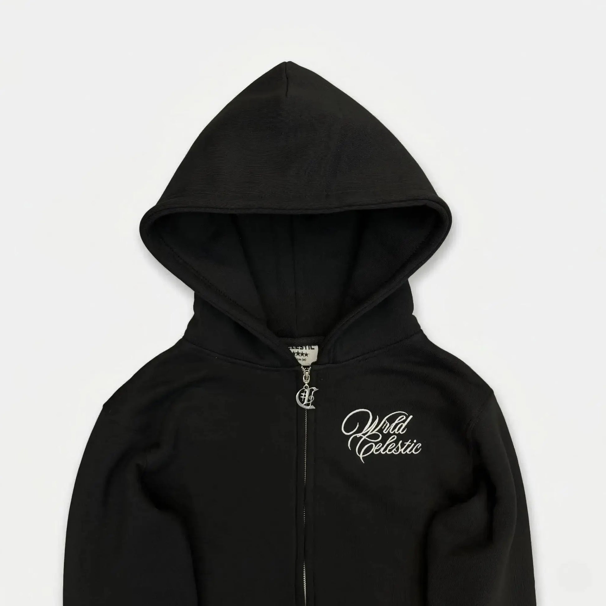 Detailed close-up view of the CELESTIC Black Basic zip-up hoodie. Highlighting the premium heavyweight black cotton fleece fabric, the structured double-lined hood, elegant white script logo embroidery on the chest, and the custom metal 'C' zipper pull.