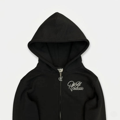 Detailed close-up view of the CELESTIC Black Basic zip-up hoodie. Highlighting the premium heavyweight black cotton fleece fabric, the structured double-lined hood, elegant white script logo embroidery on the chest, and the custom metal 'C' zipper pull.