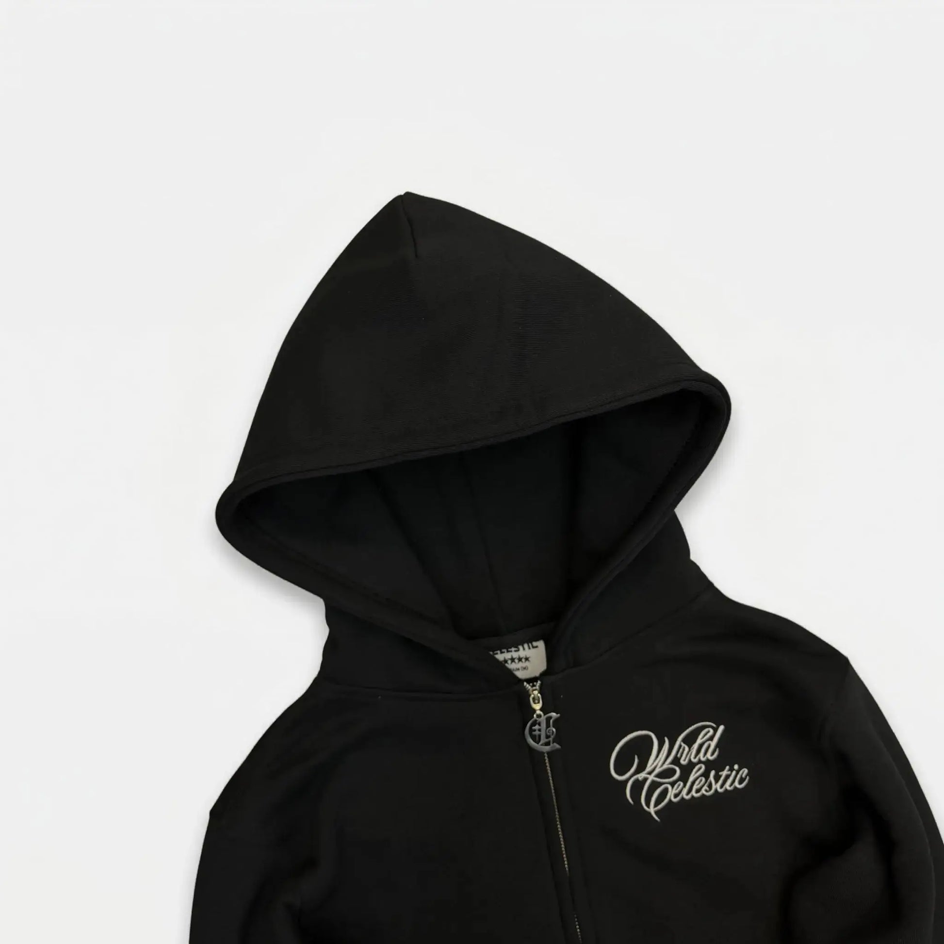 Detailed close-up of the CELESTIC Black Basic zip-up hoodie upper section. Highlighting the structured double-lined hood, premium heavyweight black cotton fleece, white script logo embroidery on the chest, and the custom metal 'C' zipper pull.