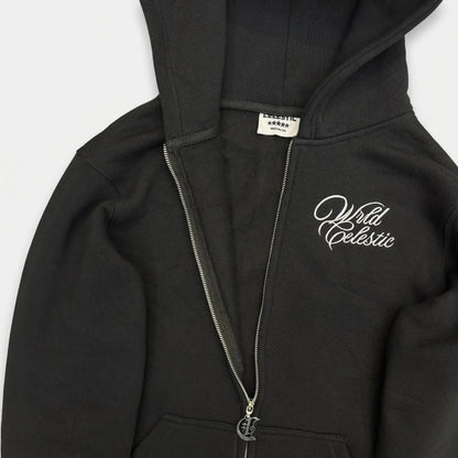 Detailed close-up of the CELESTIC Black Basic zip-up hoodie, partially unzipped to show the soft inner fleece lining and white woven neck label. Highlighting the premium heavyweight black cotton fabric, the custom silver metal 'C' zipper pull, and the elegant white script logo embroidery on the chest.