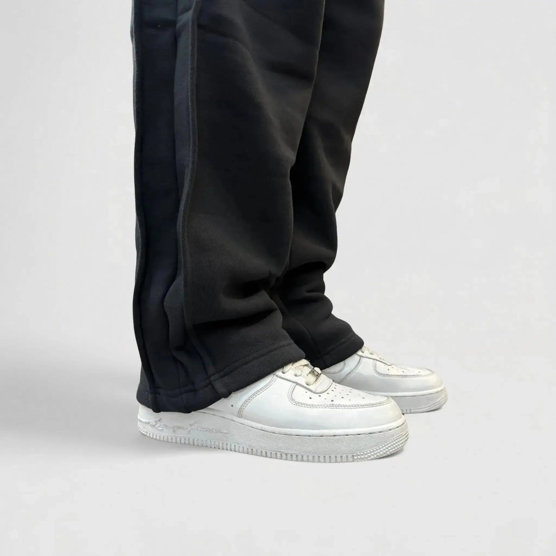 Detailed close-up view of the bottom leg on the CELESTIC Black Basic sweatpants. Highlighting the relaxed straight-leg hem, prominent side panel seams, and the premium heavyweight black cotton fleece fabric resting on white sneakers.