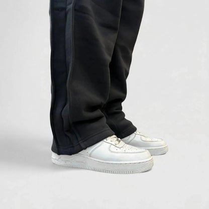 Detailed close-up view of the bottom leg on the CELESTIC Black Basic sweatpants. Highlighting the relaxed straight-leg hem, prominent side panel seams, and the premium heavyweight black cotton fleece fabric resting on white sneakers.