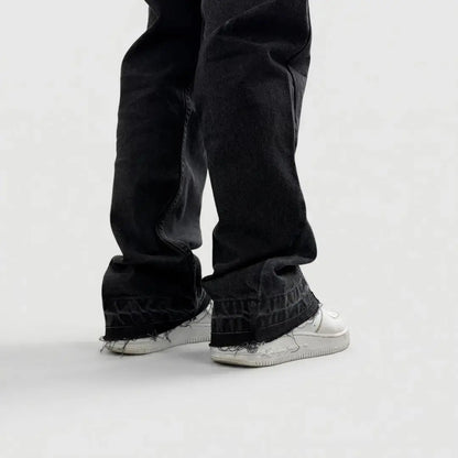 A detailed close-up rear view of the lower leg and hem of the CELESTIC Black Flared Denim Jeans on a white background. The image focuses on the intricate panelled construction of the flared leg and the heavily distressed, raw frayed edges at the bottom. The washed black denim texture is clearly visible as the fabric stacks over a white sneaker, showcasing the premium streetwear design.