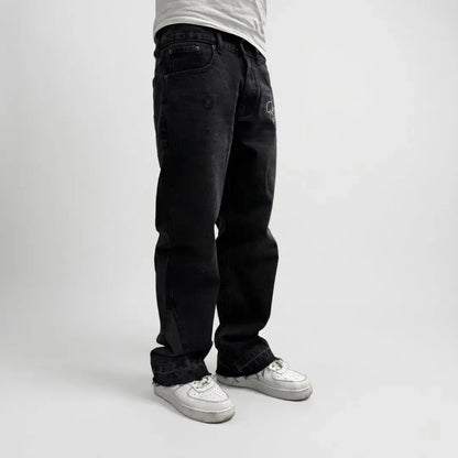 On-body side profile view of the CELESTIC Black Flared Denim Jeans on a white background. The image showcases the relaxed streetwear silhouette, the premium black washed denim fabric, and the distinctive flared leg opening with raw, frayed edges. The jeans are styled with white sneakers, highlighting the way the fabric stacks and drapes over the footwear.