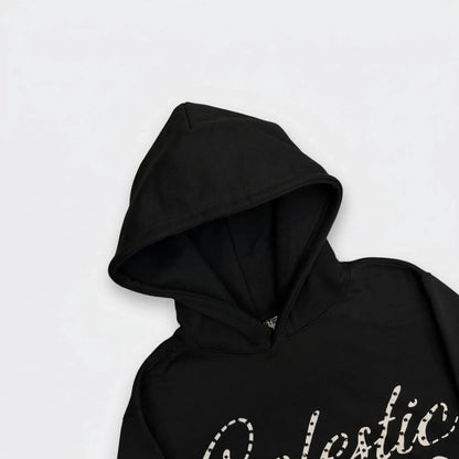 A detailed close-up photograph focusing on the hood of the CELESTIC Black Gemstone Hoodie on a white background. The image highlights the structured double-lined hood and the premium heavyweight black cotton fleece fabric. The top portion of the white screen-printed 'Celestic' script logo, beautifully embellished with sparkling rhinestones, is visible on the upper chest.