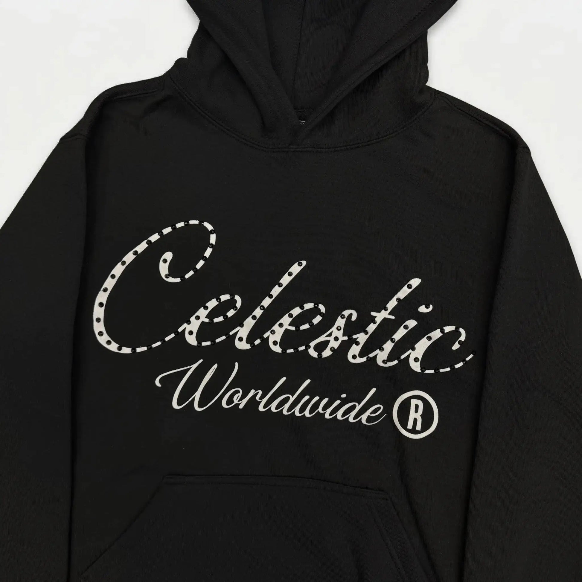 Detailed close-up photograph of the CELESTIC Black Gemstone Hoodie. The focus is on the chest, showcasing the premium heavyweight black cotton fleece and the large white screen-printed 'Celestic' script logo, heavily detailed with sparkling rhinestones. The white printed text 'Worldwide ®' is clearly visible below the script. The base of the structured hood and the top of the kangaroo pocket frame the logo.