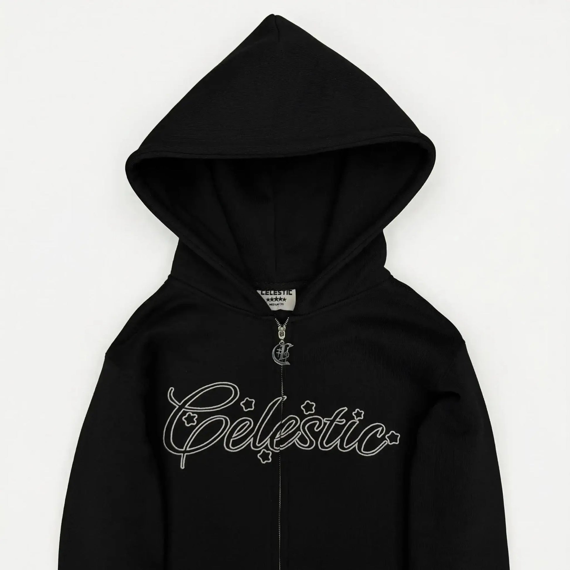 Black oversized zip-up hoodie detailed close-up view on model. Highlights include the full-length metal zipper, spacious front kangaroo-style pockets, and the ribbed hem and cuff structure. The premium heavyweight fleece cotton texture is clearly visible against a concrete background.