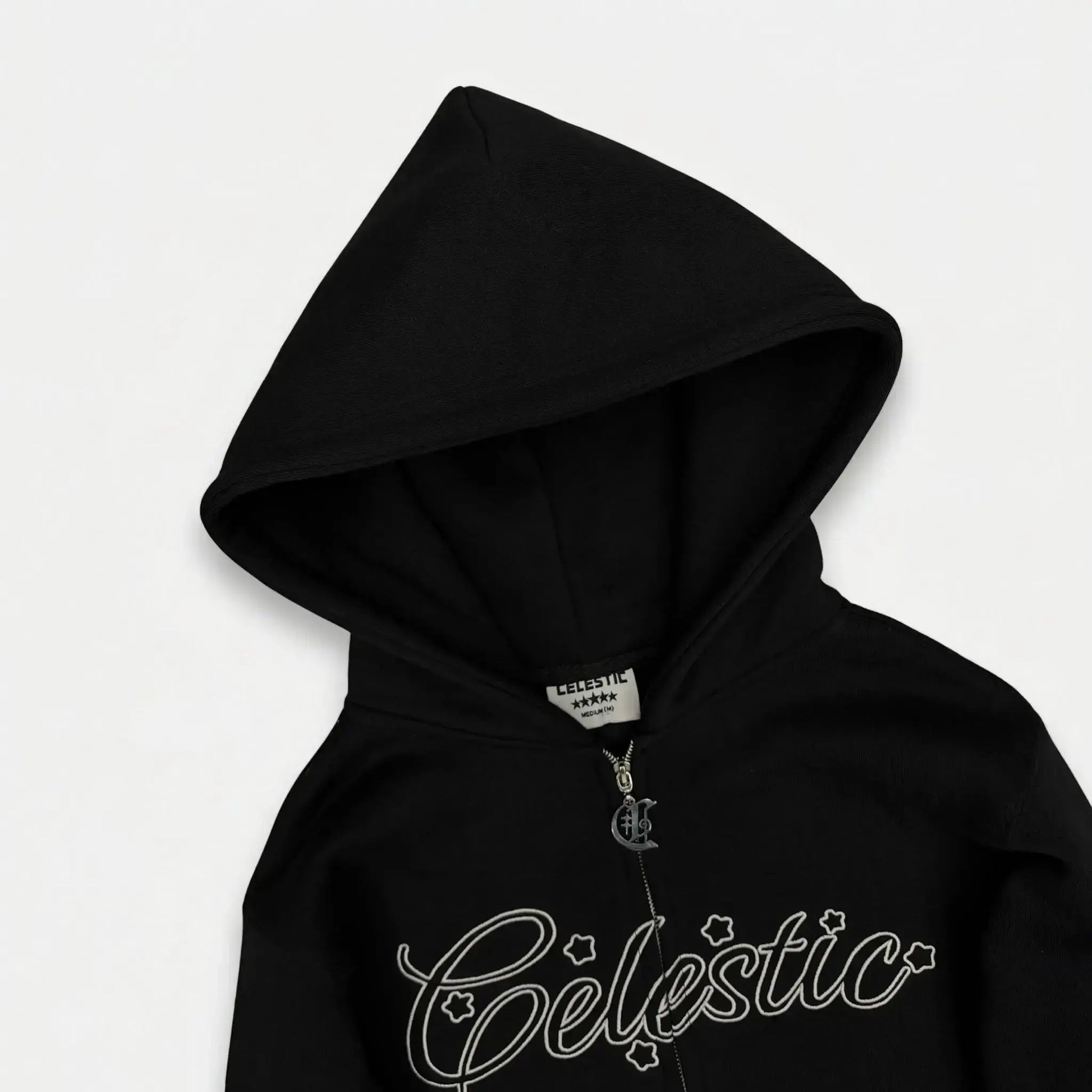 Black oversized zip-up hoodie detailed close-up of the hood and chest. Highlighting the structured double-lined hood, custom metal 'C' logo zipper pull, inner neck brand label, and the signature Celestic white outline embroidery with star accents on premium heavyweight fleece.