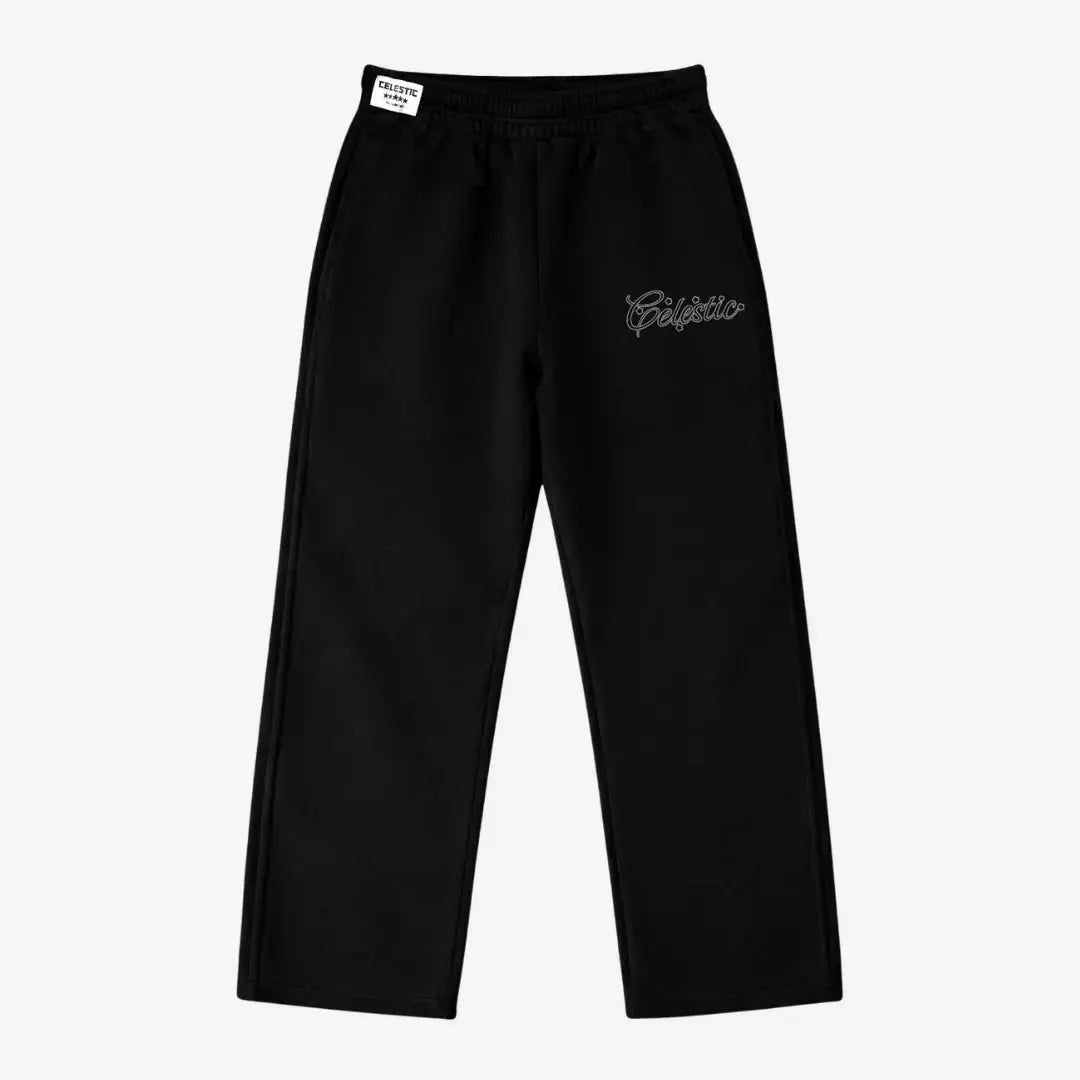 Black oversized tracksuit sweatpants laid flat on a white background. The premium heavyweight cotton fleece pants feature an elasticated waistband with a woven Celestic brand label, and the signature white outline logo embroidery with star accents on the left thigh.