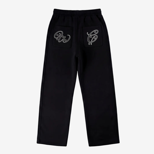 Black oversized tracksuit sweatpants back view laid flat on a white background. The premium heavyweight cotton fleece pants feature an elasticated waistband and custom white outline logo embroidery with star accents on both back pockets.