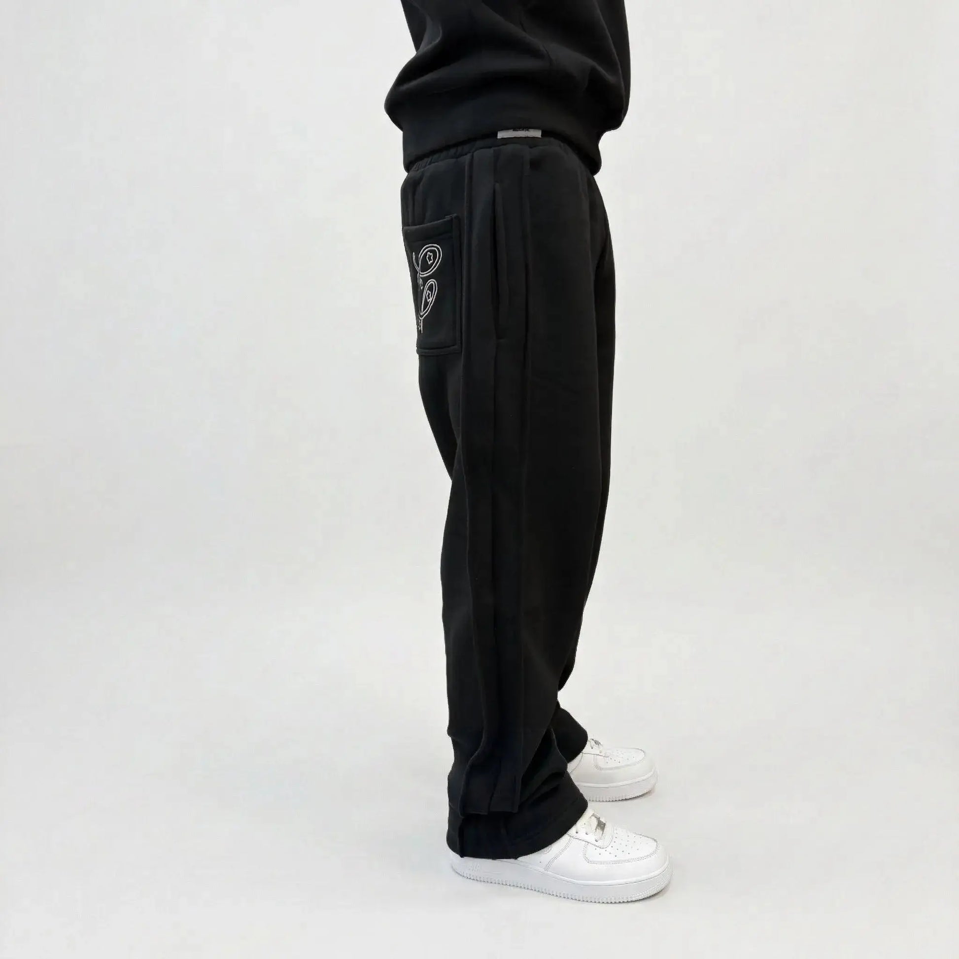 Black oversized tracksuit sweatpants detailed close-up of waistband and pocket. On-model shot highlighting the elastic waist, black internal drawstring cord, deep side pocket, white contrast stitching, and premium heavyweight fleece texture against concrete background.