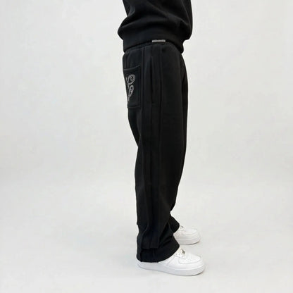 Black oversized tracksuit sweatpants detailed close-up of waistband and pocket. On-model shot highlighting the elastic waist, black internal drawstring cord, deep side pocket, white contrast stitching, and premium heavyweight fleece texture against concrete background.