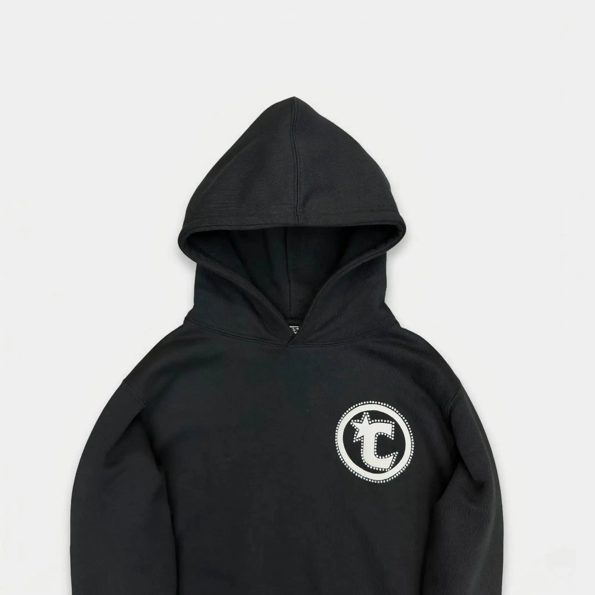 Detailed close-up of the CELESTIC Black Star hoodie upper section. Highlighting the premium heavyweight black cotton fleece fabric, the structured double-lined hood, and the prominent white circular 'C' star logo embroidery on the chest.