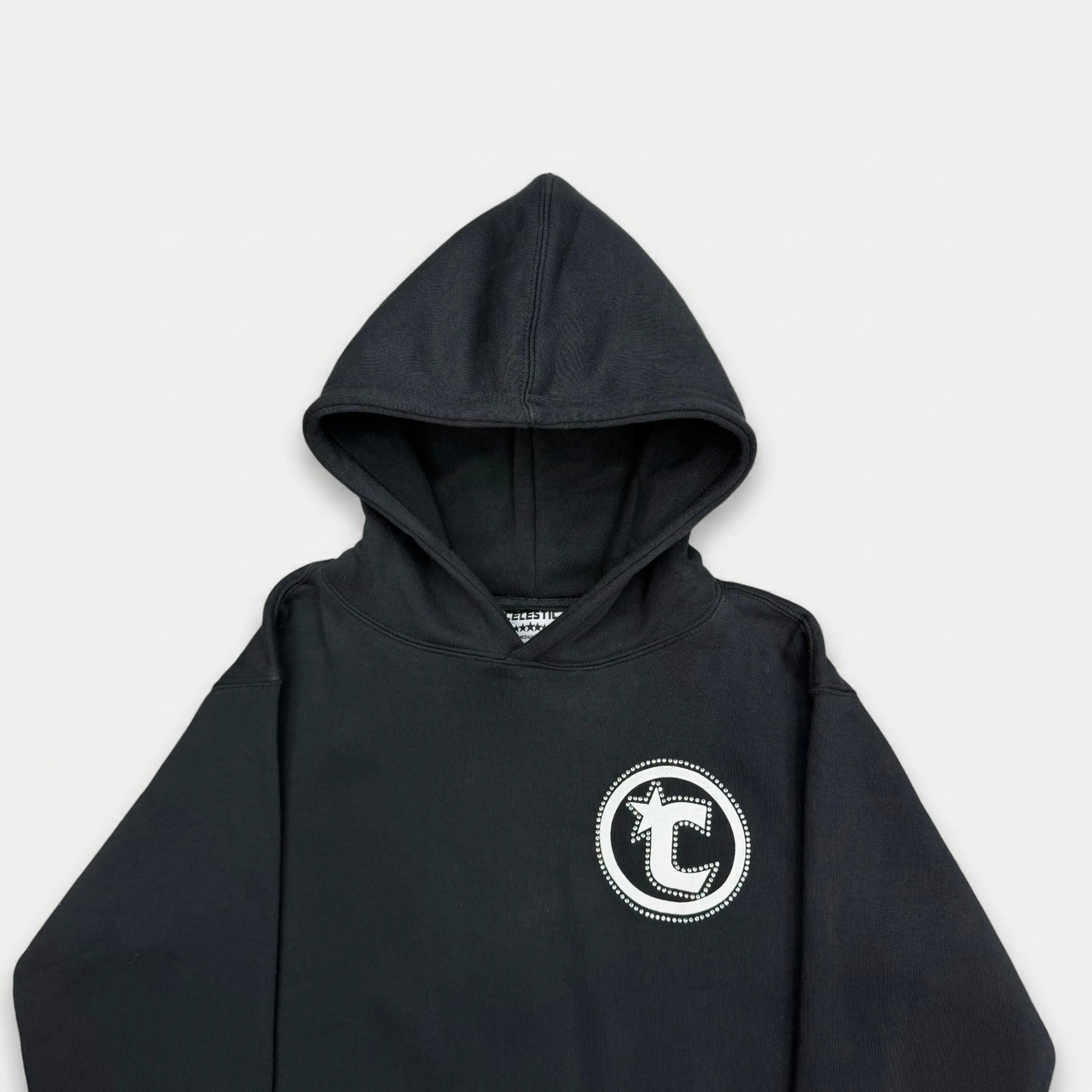 Detailed close-up of the CELESTIC Black Star hoodie upper section. Highlighting the premium heavyweight black cotton fleece fabric, the structured double-lined hood, and the prominent white circular 'C' star logo embroidery on the chest.