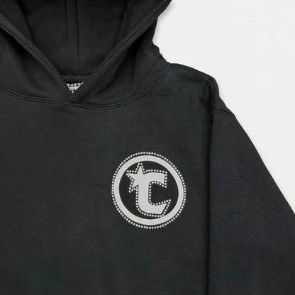 Extreme close-up of the CELESTIC Black Star Hoodie. Highlighting the prominent circular white 'C' star logo embroidery on the left chest with its intricate dotted border detail, set against the premium heavyweight black cotton fleece fabric texture.