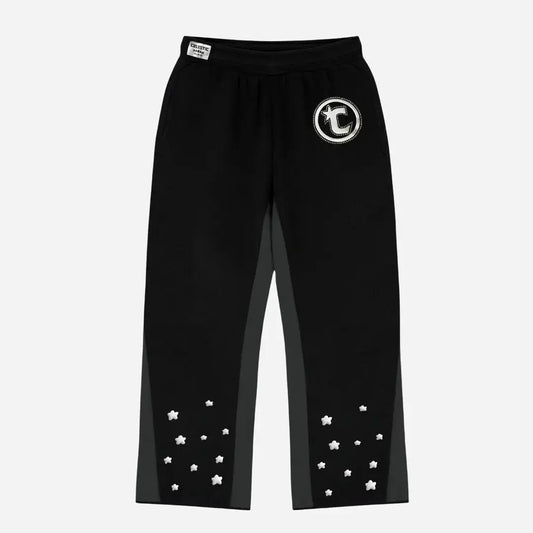 Front view flat-lay photograph of the CELESTIC Black Star Pants on a white background. These premium heavyweight black cotton fleece sweatpants feature a relaxed straight-leg fit, contrasting grey side panels, and multiple scattered white embroidered stars on the lower legs. Details include a prominent white circular 'C' star logo embroidery on the left thigh and a woven CELESTIC brand label on the elastic waistband.