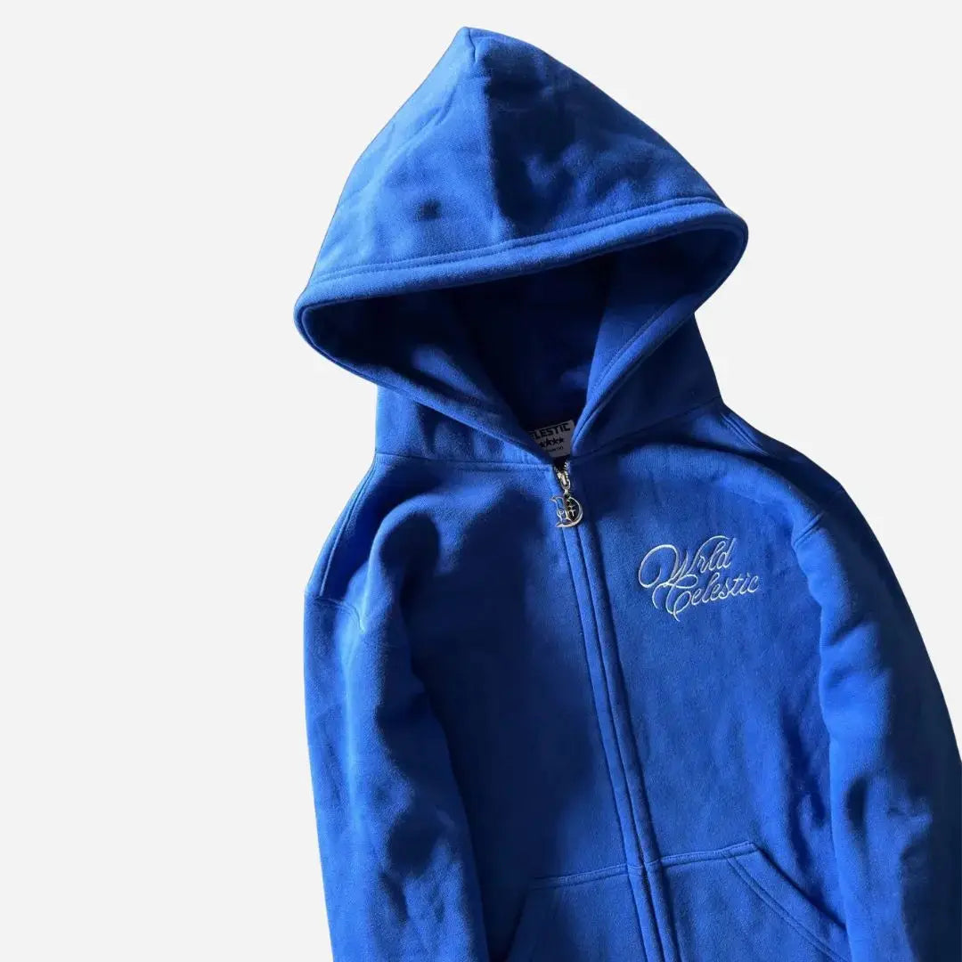 Angled close-up of the CELESTIC Blue Basic zip-up hoodie. Highlighting the structured double-lined hood, the elegant white script logo embroidery on the chest, and the custom metal 'C' zipper pull against the premium heavyweight blue fleece.