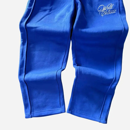 Detailed close-up of the lower legs and hems of the CELESTIC Blue Basic sweatpants. Highlighting the relaxed straight fit with an open hem, prominent side panel seams, and the elegant white script logo embroidery on the thigh against the premium heavyweight blue fleece.