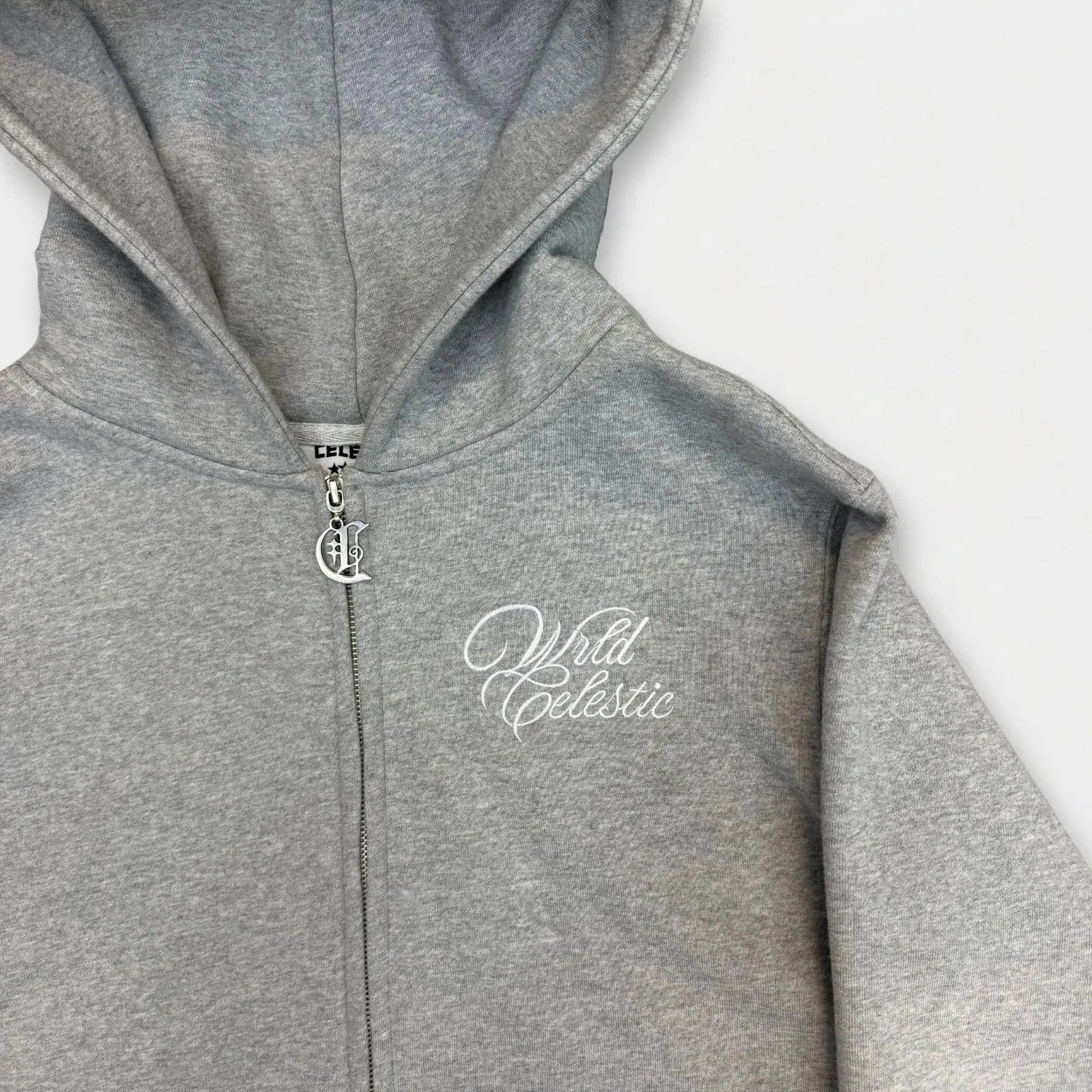 Detailed close-up of the CELESTIC Grey Basic zip-up hoodie chest. Highlighting the premium heavyweight grey cotton fleece texture, the elegant white script logo embroidery, and the custom silver metal 'C' zipper pull.