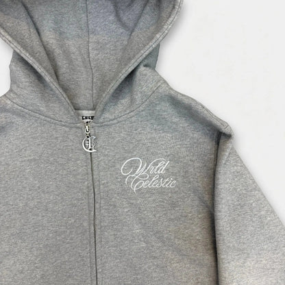 Detailed close-up of the CELESTIC Grey Basic zip-up hoodie chest. Highlighting the premium heavyweight grey cotton fleece texture, the elegant white script logo embroidery, and the custom silver metal 'C' zipper pull.