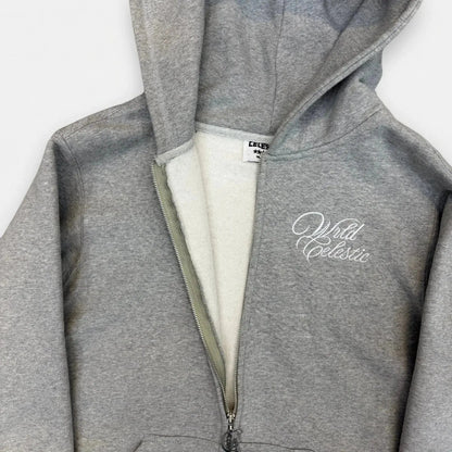 Detailed close-up of the CELESTIC Grey Basic zip-up hoodie, partially unzipped to show the soft inner fleece lining. Highlighting the premium heavyweight grey cotton fabric, the custom metal 'C' zipper pull, and the elegant white script logo embroidery on the chest.