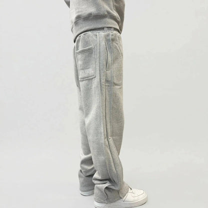 Back angle view of a model wearing the CELESTIC Grey Basic sweatpants. These premium heavyweight grey cotton fleece pants feature a relaxed straight-leg silhouette, white 'WORLDWIDE' embroidery on the right back pocket, and prominent side panel seams. Shown with white sneakers on a clean light background.