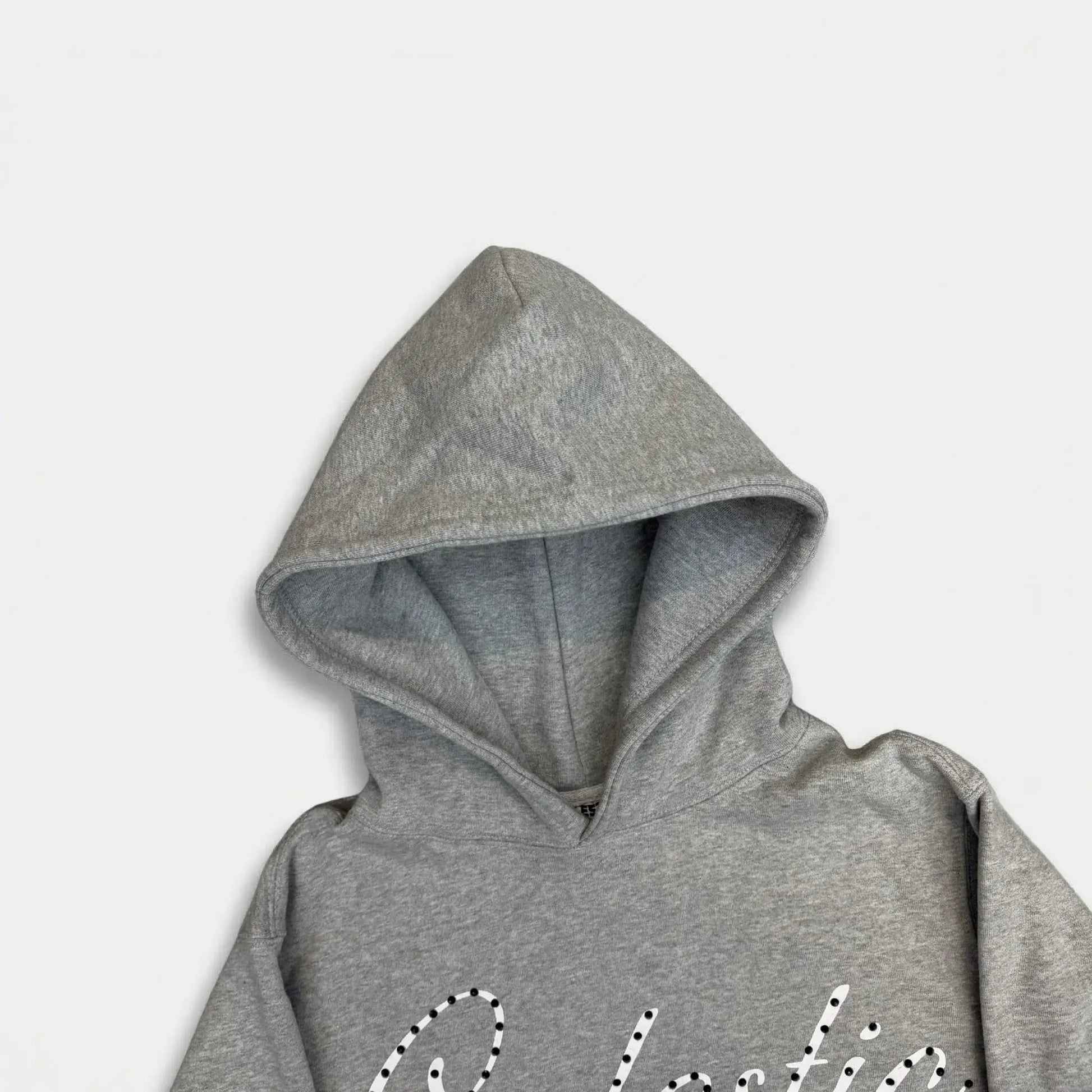 A detailed close-up photograph focusing on the hood of the CELESTIC Grey Gemstone Hoodie on a white background. The image highlights the structured double-lined hood and the premium heather grey cotton fleece fabric. The top portion of the white screen-printed 'Celestic' script logo, beautifully embellished with sparkling rhinestones, is visible on the upper chest.