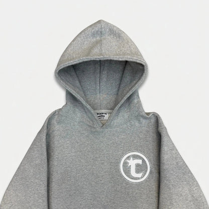 Front view flat-lay photograph of the CELESTIC Grey Star Hoodie on a white background. This premium heather grey cotton fleece pullover hoodie features light grey side panels and a spacious kangaroo pocket. A large white circular 'C' star logo is screen-printed on the left chest. The sleeves and lower body show white embroidered star details. A white woven brand label is visible on the inner neck.