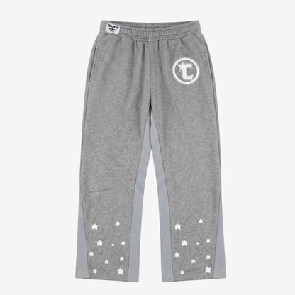 Front view flat-lay photograph of the CELESTIC Grey Star Pants on a white background. These premium heather grey cotton fleece sweatpants feature light grey side panels and a relaxed fit. A white circular 'C' star logo is featured on the left thigh, while the lower legs are detailed with multiple scattered white embroidered stars. A white woven CELESTIC brand label is visible on the elastic waistband.