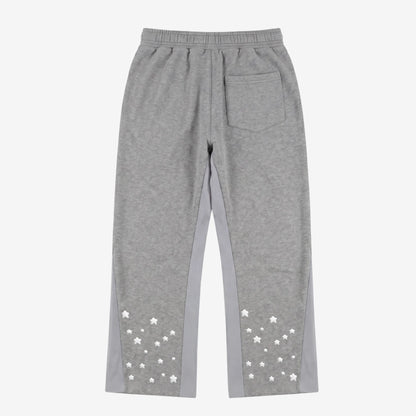 Back view flat-lay photograph of the CELESTIC Grey Star Pants on a white background. These premium heather grey cotton fleece sweatpants feature light grey side panels, a relaxed fit, and a single back pocket on the right side. The lower back of both legs is detailed with multiple scattered white embroidered stars, highlighting the unique streetwear aesthetic of the Star collection.