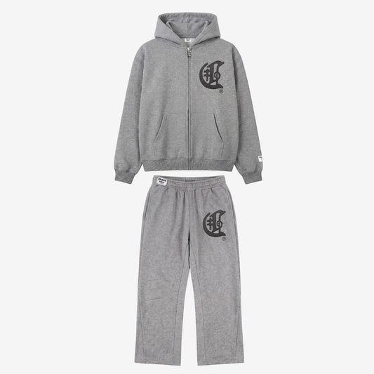 Full front view flat-lay photograph of the CELESTIC Grey Zipper Tracksuit on a white background. The set includes a premium heather grey zip-up hoodie with a kangaroo pocket and a matching pair of relaxed-fit sweatpants. Both pieces feature a large, distinctive black gothic-style 'C' star logo on the left chest and left thigh. The hoodie has a woven brand patch on the left sleeve, and the pants include a matching label on the waistband.