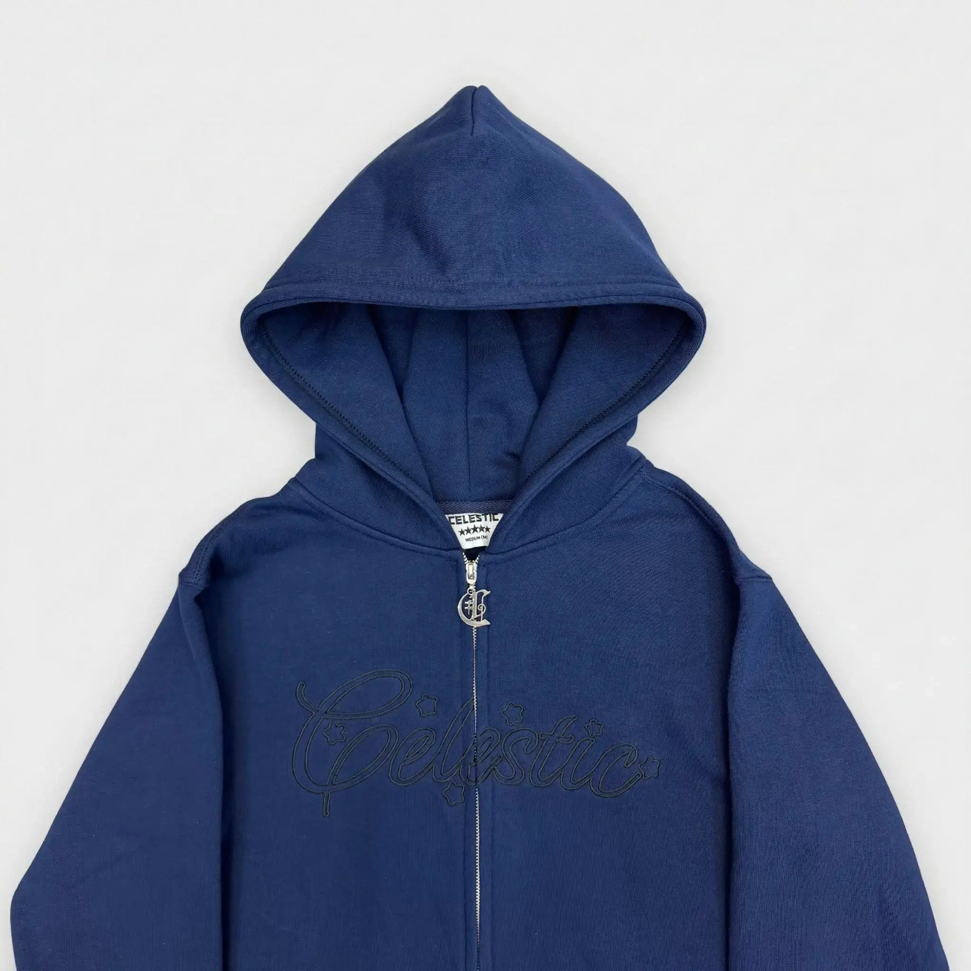 Detailed close-up view of the chest area of the CELESTIC Navy Blue Outline zip-up hoodie. Highlighting the large tonal 'Celestic' outline logo embroidery across the chest, the custom metal 'C' zipper pull, and the structured double-lined hood on premium heavyweight navy blue cotton fleece.