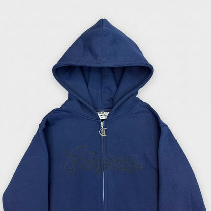 Detailed close-up view of the chest area of the CELESTIC Navy Blue Outline zip-up hoodie. Highlighting the large tonal 'Celestic' outline logo embroidery across the chest, the custom metal 'C' zipper pull, and the structured double-lined hood on premium heavyweight navy blue cotton fleece.