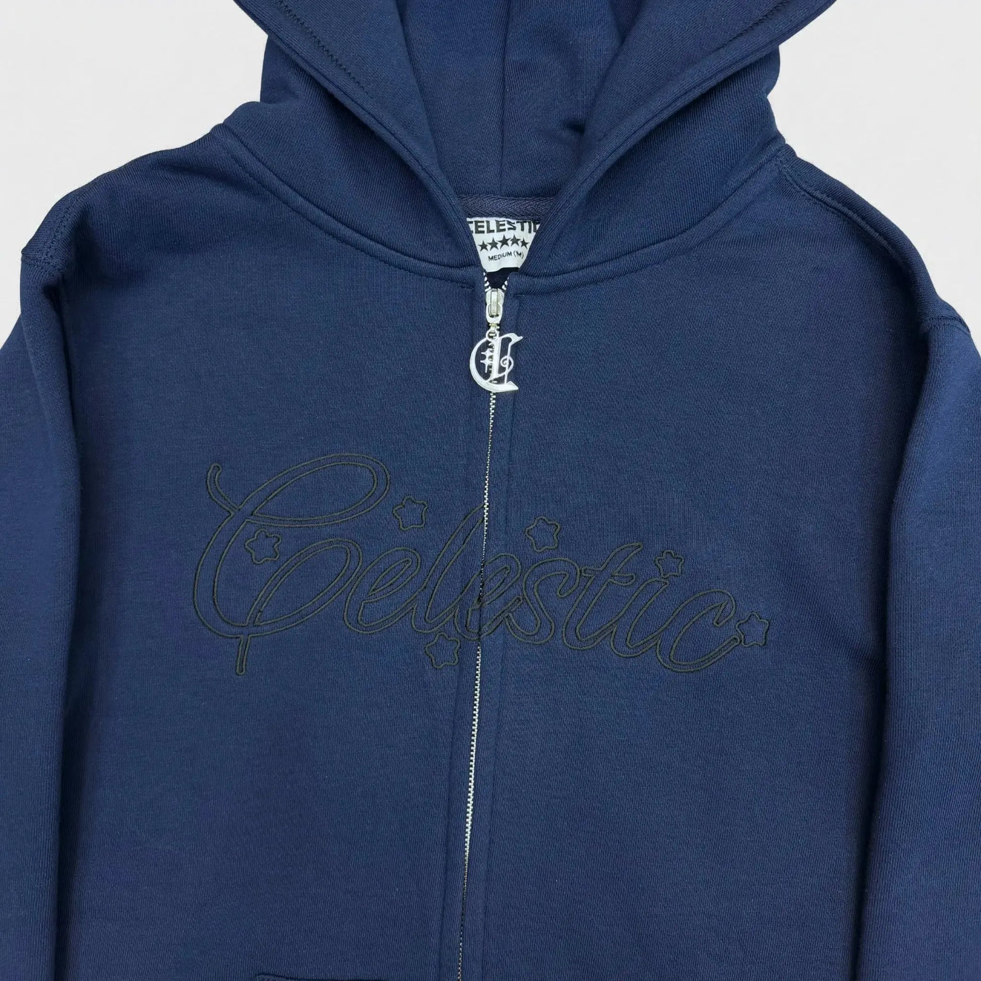 Detailed close-up of the chest on the CELESTIC Navy Blue Outline zip-up hoodie. Highlighting the large tonal 'Celestic' outline embroidery with subtle star details, the custom silver metal 'C' zipper pull, and the premium heavyweight navy blue cotton fleece material.