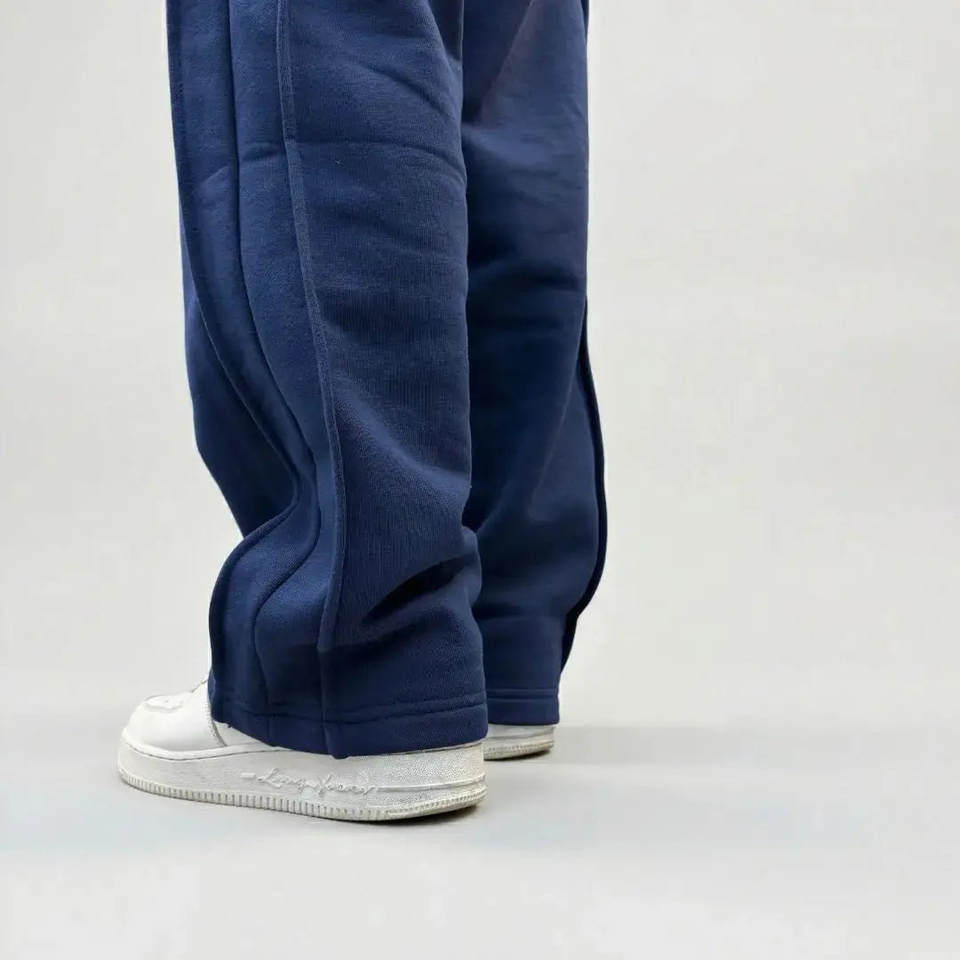 Detailed back-angle close-up of the bottom legs on the CELESTIC Navy Blue Outline sweatpants. Highlighting the prominent raised side panel seams, the relaxed straight-leg fit, and the premium heavyweight navy blue cotton fleece fabric pooling over white sneakers.