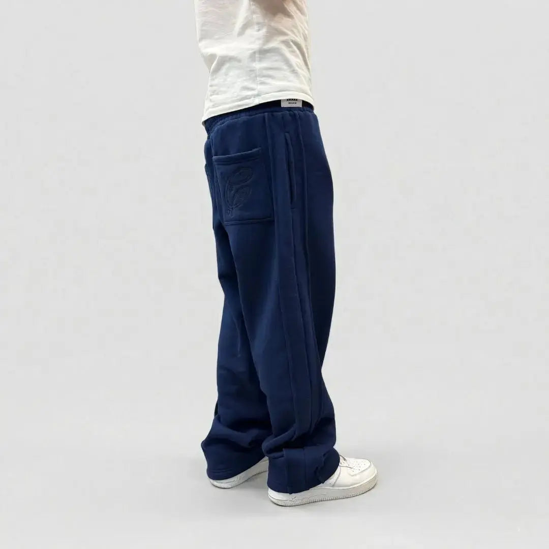 Back angle view of a model wearing the CELESTIC Navy Blue Outline sweatpants. These premium heavyweight cotton fleece pants feature a relaxed straight-leg silhouette, tonal outline embroidery on the right back pocket, and prominent side panel seams. Shown with white sneakers on a clean light background.