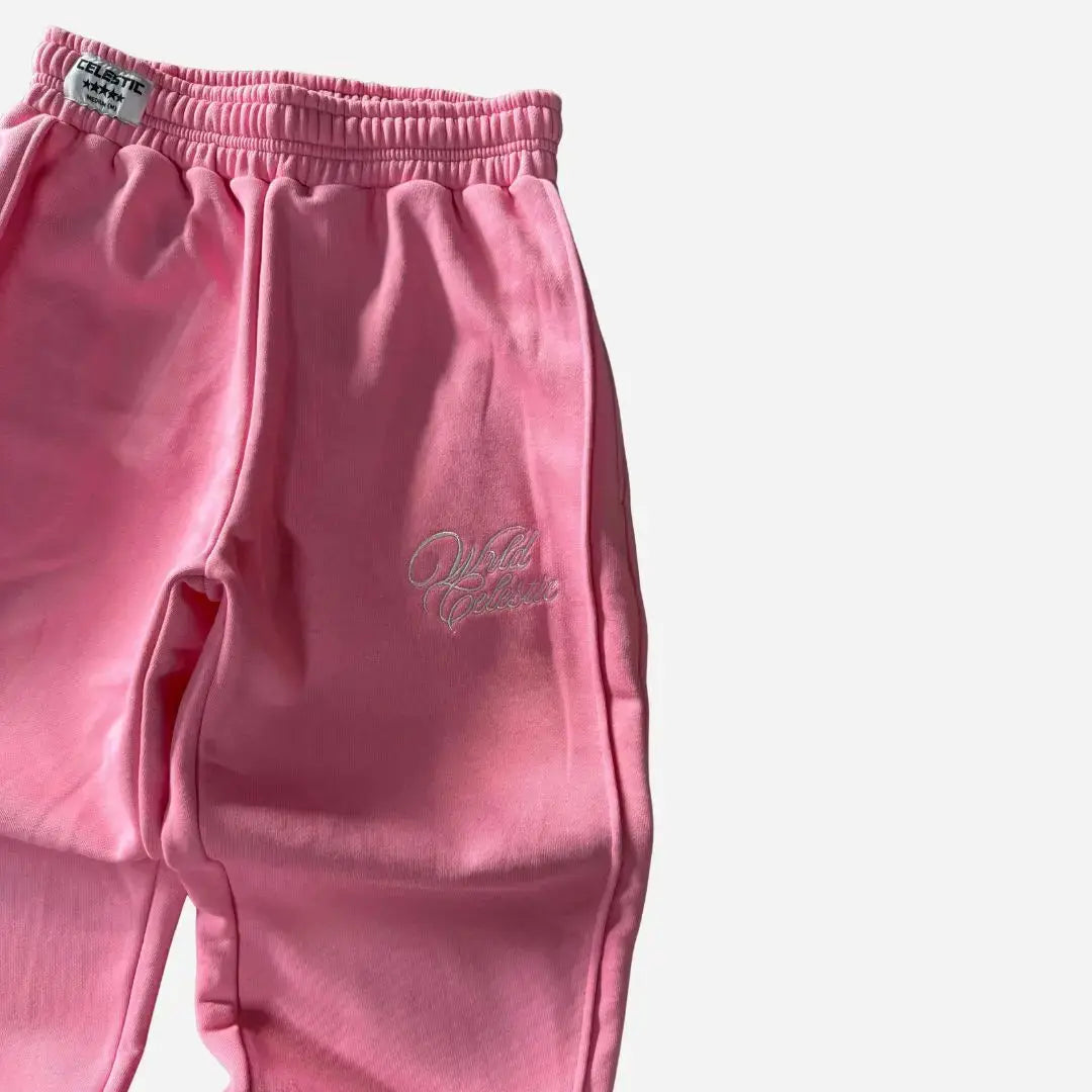 Angled close-up view of the CELESTIC Pink Basic sweatpants focusing on the left side. Highlighting the elegant white script logo embroidery on the thigh, prominent side seam detailing, and the elasticated ribbed waistband with a woven brand tag against the premium heavyweight pink fleece.