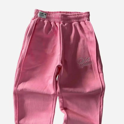 Detailed close-up of the upper front of the CELESTIC Pink Basic sweatpants. Highlighting the elasticated ribbed waistband with a woven brand tag, prominent side seams, and the elegant white script logo embroidery on the left thigh against the premium heavyweight pink fleece.
