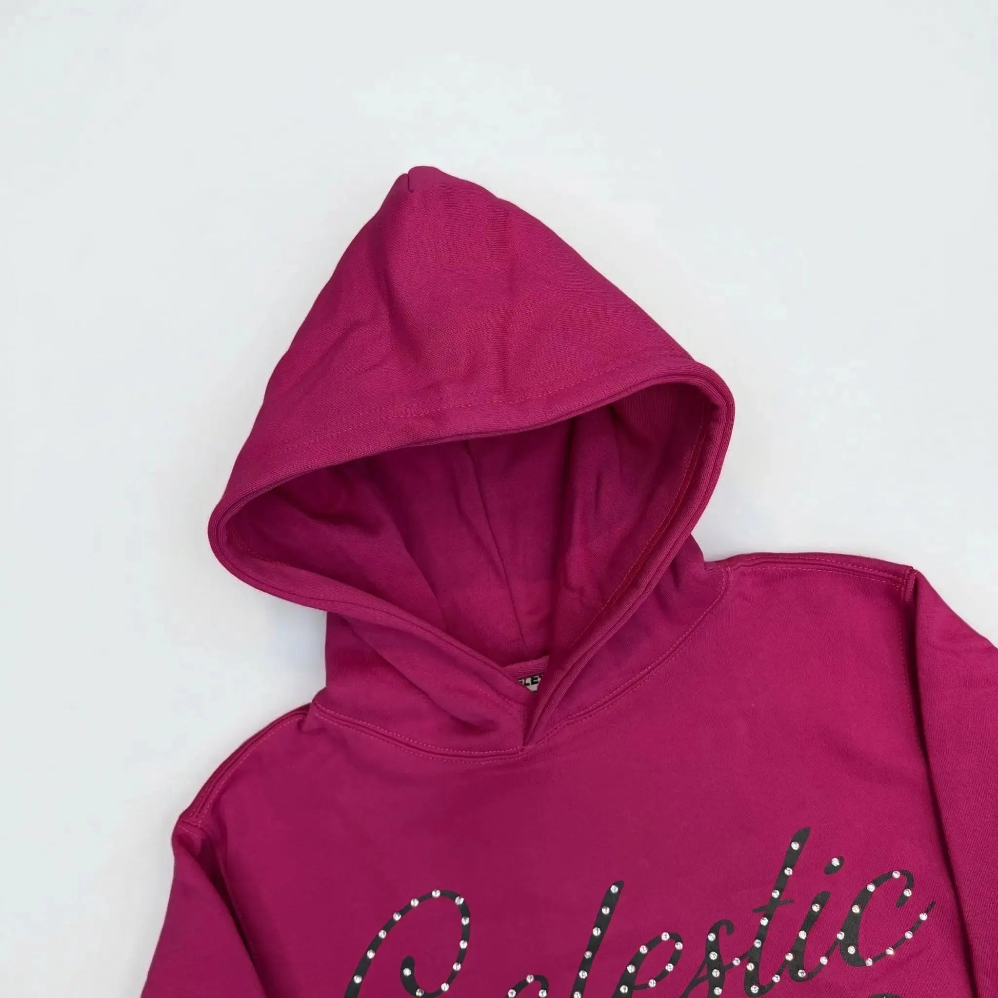 A detailed close-up photograph focusing on the hood of the CELESTIC Pink Gemstone Hoodie on a white background. The image highlights the structured double-lined hood and the premium vibrant pink cotton fleece fabric. The top portion of the black screen-printed 'Celestic' script logo, beautifully embellished with sparkling rhinestones, is visible on the upper chest.