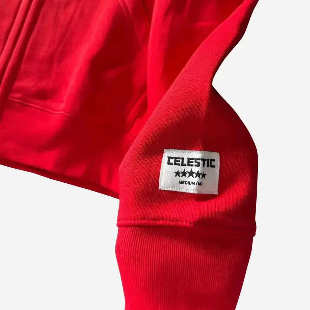 Detailed close-up of the sleeve on the CELESTIC Red Basic zip-up hoodie. Highlighting the premium heavyweight red cotton fleece, the thick ribbed cuff, and the signature white woven CELESTIC brand patch featuring five stars.