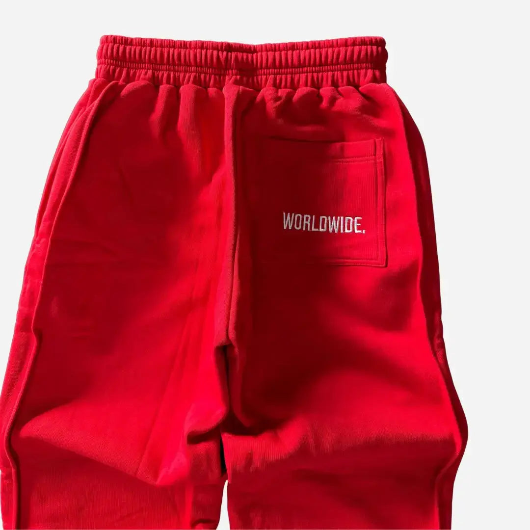 Detailed close-up of the back of the CELESTIC Red Basic sweatpants. Highlighting the right back pocket with white 'WORLDWIDE' embroidery, the elasticated ribbed waistband, and the premium heavyweight red cotton fleece fabric.
