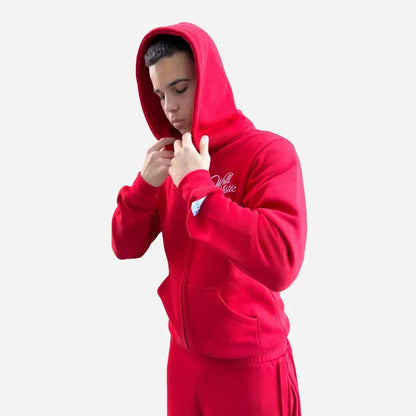 Side view of a model wearing the CELESTIC Red Basic Tracksuit with the hood up. Highlighting the premium heavyweight red fleece zip-up hoodie with white script logo embroidery on the chest and a structured double-lined hood, paired with matching red sweatpants.