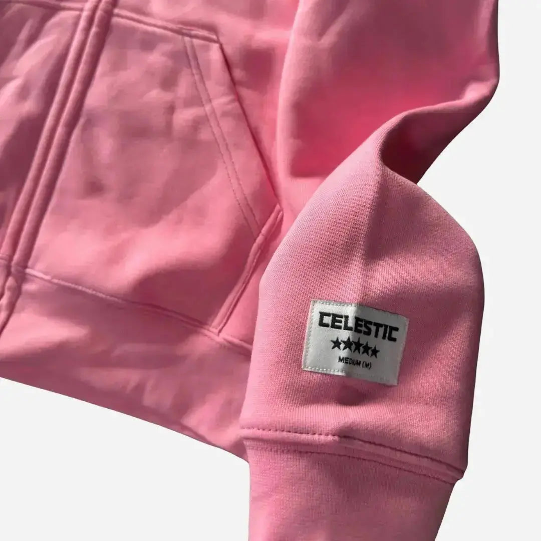 Detailed close-up view of the small woven black tag on the outer left sleeve of the Celestic Basic black hoodie. Highlighting the precise stitching, the white embossed 'C' logo with a star pattern, and the text 'CELESTIC BASIC' with 'EST. 2021' in clean, white sans-serif font. The rich black fleece fabric texture is visible.