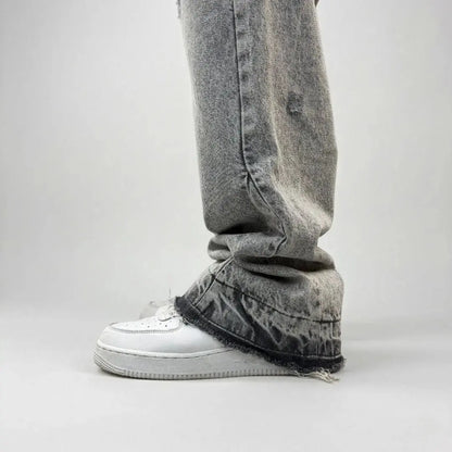Grey flared jeans detailed close-up of the lower leg and hem. Washed distressed denim pants highlighting the perfect stacking over white sneakers, featuring a frayed raw hem, subtle rip detail, and leg panel stitching.