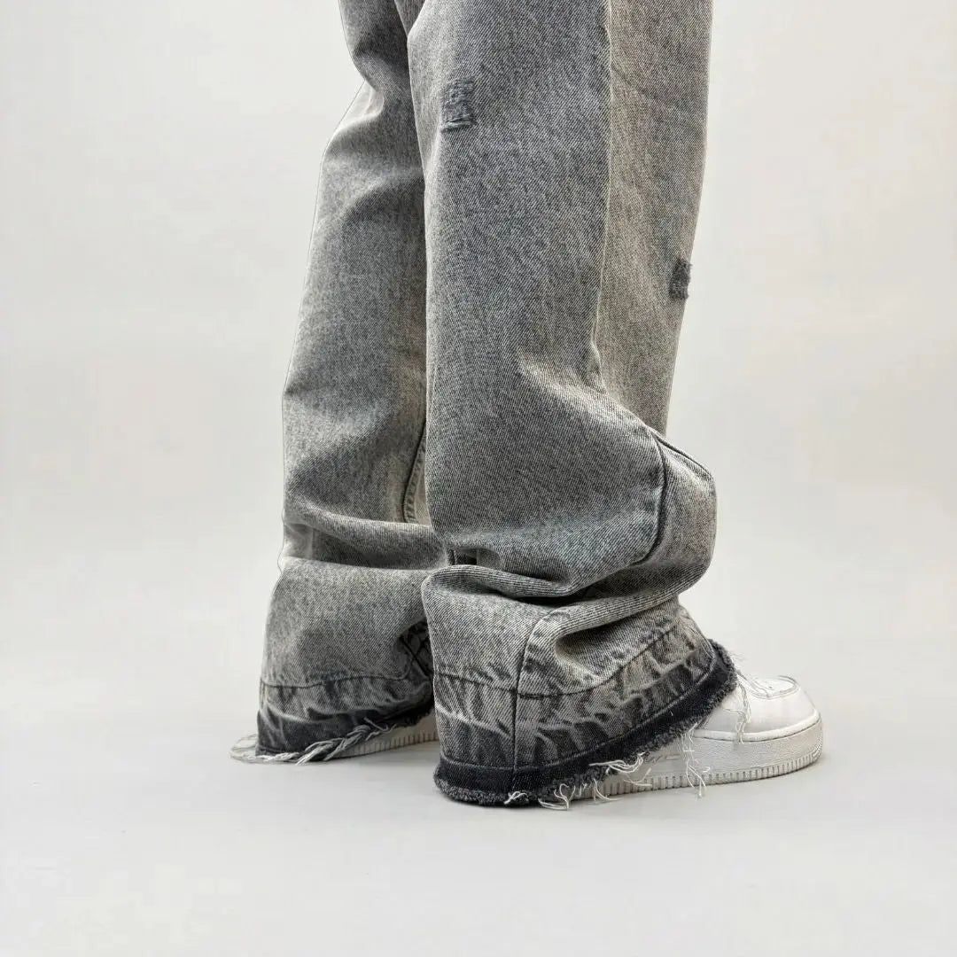 Grey flared jeans detailed back angle close-up of the lower leg and hem. Washed distressed denim pants highlighting the back leg panel stitching, frayed raw hem, and the relaxed fit stacking effortlessly over white sneakers.