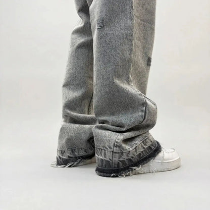 Grey flared jeans detailed back angle close-up of the lower leg and hem. Washed distressed denim pants highlighting the back leg panel stitching, frayed raw hem, and the relaxed fit stacking effortlessly over white sneakers.