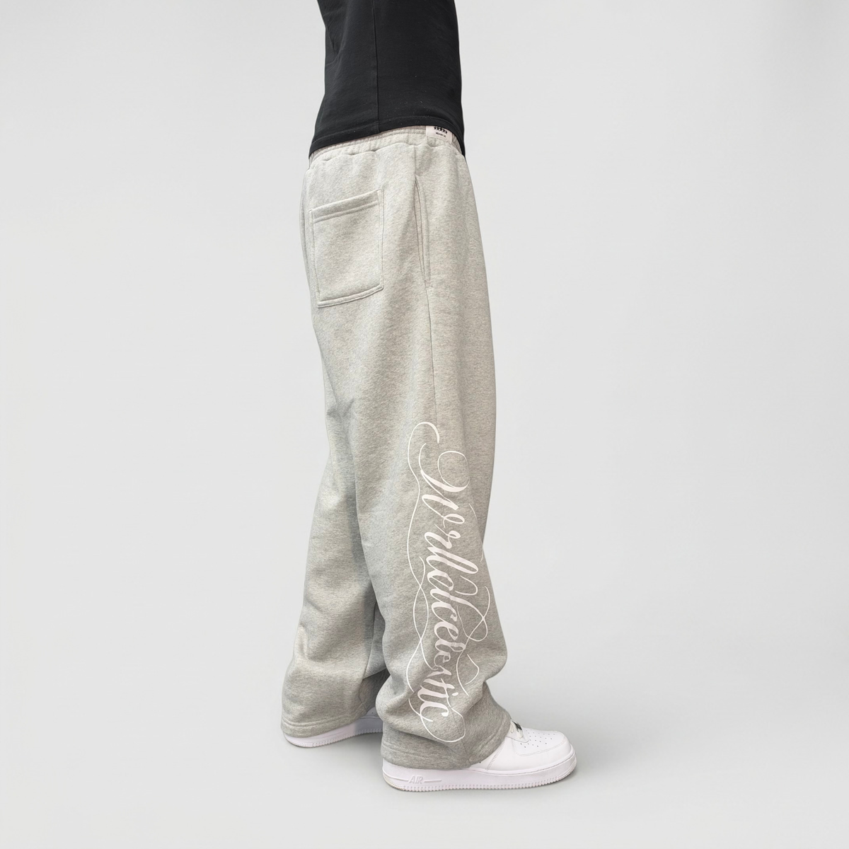 Side view on model of the CELESTIC Grey Script Pants, showing the white Wrldcelestic script print running down the leg.